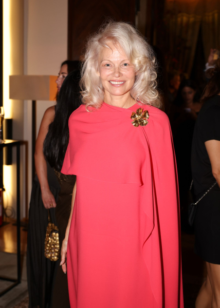 Pamela Anderson smiles in a pink dress and fluffy curls.